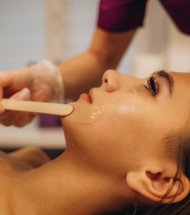 Cosmetologist applying mask on woman's face in spa salon, above view